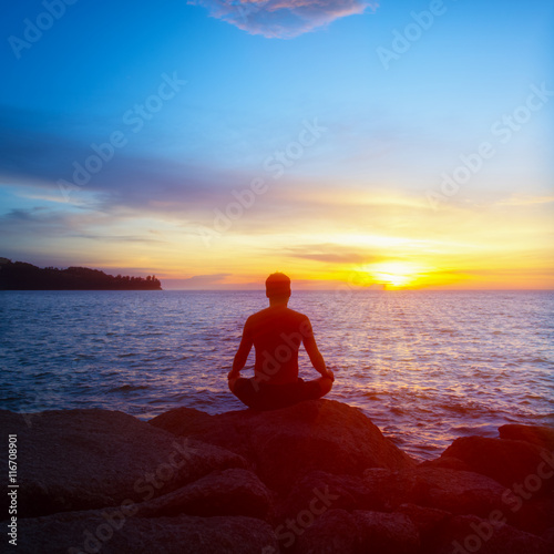 Young man practices yoga on the beach at sunset