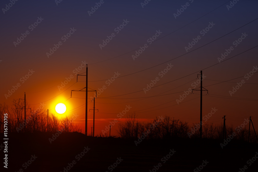 Poles of power lines at sunset - industrial landscape
