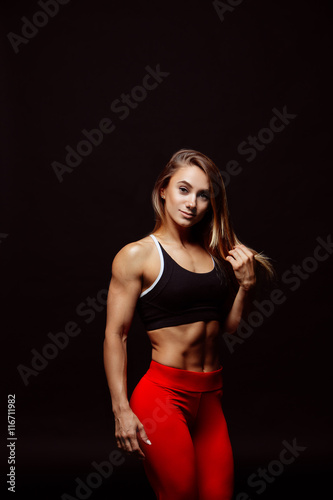 Image of muscular young woman posing in sportswear against black