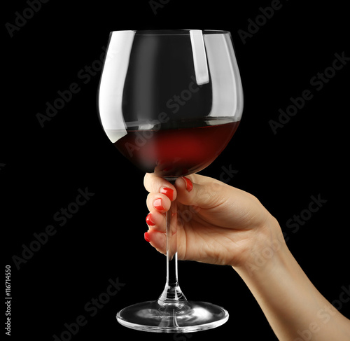 Female hand holding glass of wine on black background