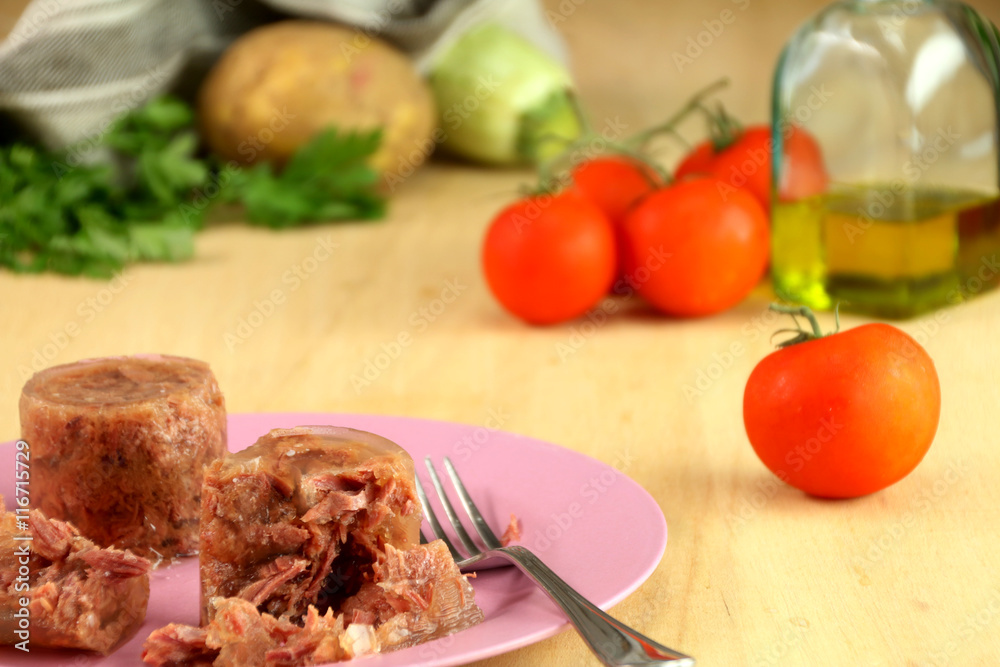 A pink dish with famous italian leancheon meat. Background: tomatoes, potato, zucchini, parsley, a bottle of olive oli and a linen cloth. A pink dish with famous italian leancheon meat. Background: tomatoes, potato, zucchini, parsley, a bottle of olive oli and a linen cloth.