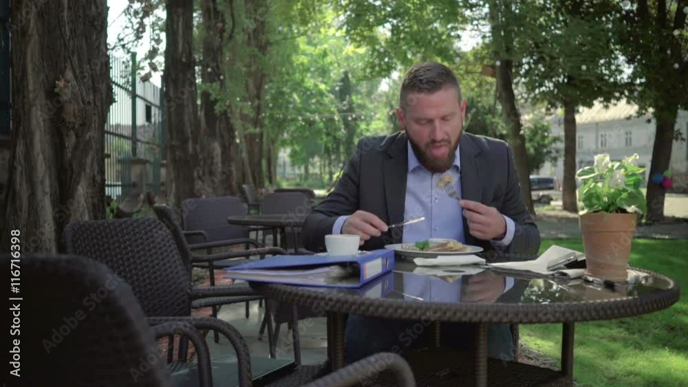 Businessman answers the phone and checks data during lunch. Steadicam shot.
