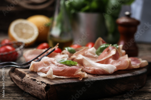 thin slices of prosciutto with mixed with basil, cherry tomatoes on wooden cutting board,vintage background