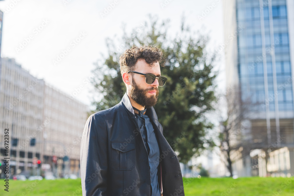 Half length of young handsome black hair bearded caucasian modern businessman wearing sunglasses outdoor in the city, pensuive - serious, thoughtful, thinking future concept Half length of young handsome black hair bearded caucasian modern businessman wearing sunglasses outdoor in the city, pensuive - serious, thoughtful, thinking future concept
