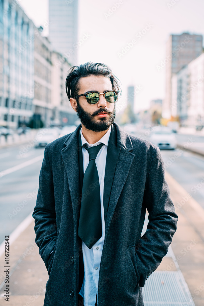 Half length of young handsome caucasian bearded businessman posing outdoor in the street, overlooking pensive wearing sunglasses - business, thoughtful, serious concept