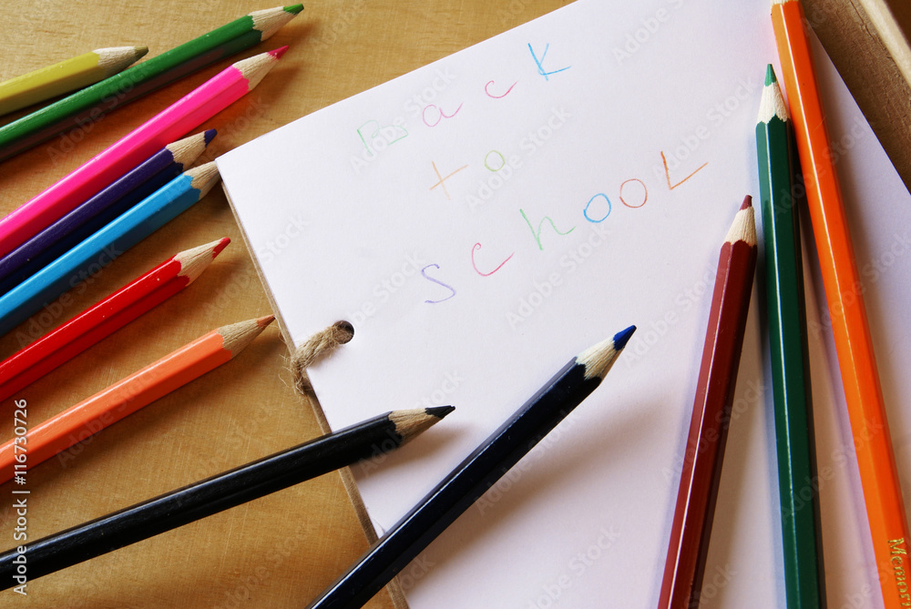 Back to school. Notepad on the table, along with colored pencils, lying on it randomly. Bright colors. Back to school. Notepad on the table, along with colored pencils, lying on it randomly. Bright colors.