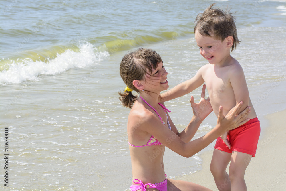 On the beach elder sister wants to hug a baby brother, and against the backdrop of the sea waves On the beach elder sister wants to hug a baby brother, and against the backdrop of the sea waves