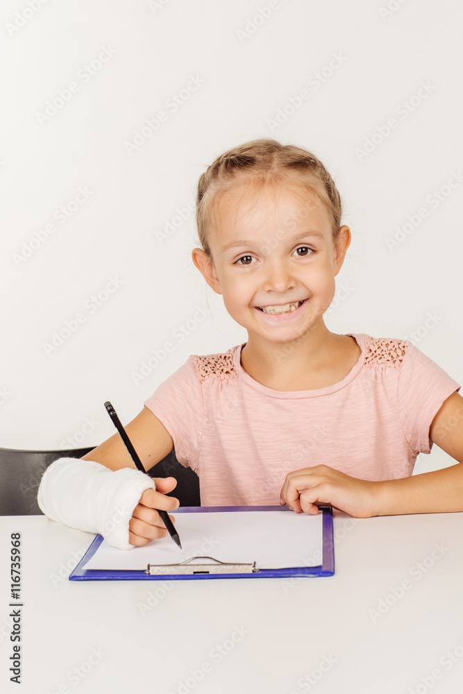 Pretty little girl with broken arm is smiling, sitting at the table Pretty little girl with broken arm is smiling, sitting at the table