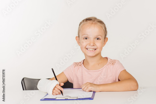 smiling little girl with broken arm is sitting at the table