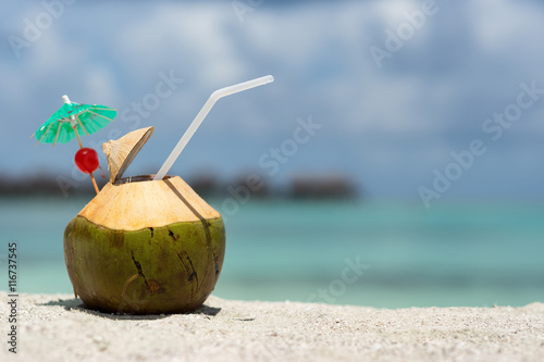 Coconut with drinking straw on beach at the sea