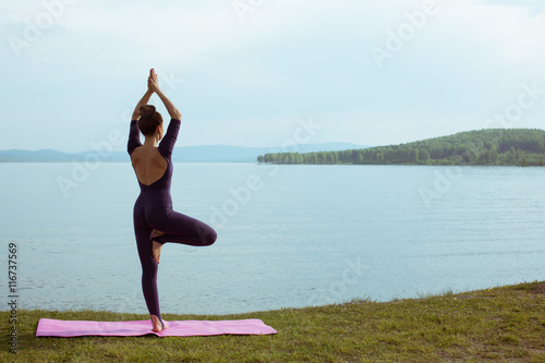Young woman is practicing yoga at mountain lake