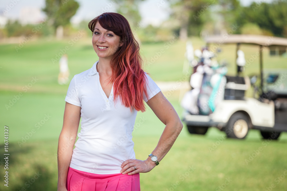 Young woman standing in front of golf cart on golf course with b Young woman standing in front of golf cart on golf course with b