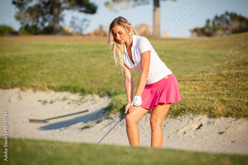 Beautiful young girl playing golf in sand trap on course.