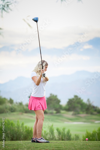 Blonde female golfer swinging club on golf course green with cop