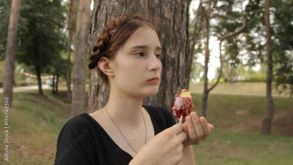 Beatiful girl eats candy apple. Zoom in and out.