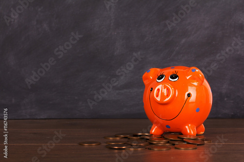 Coins and orange piggy bank on a wooden surface