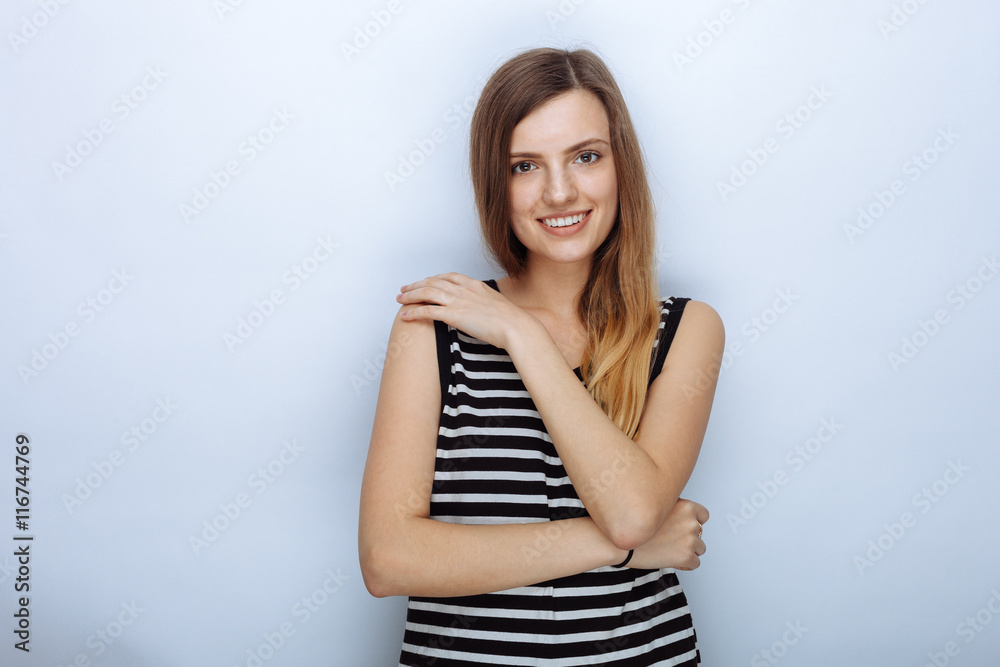 Portrait of happy young beautiful woman in striped shirt hugging herself posing for model tests against white studio background