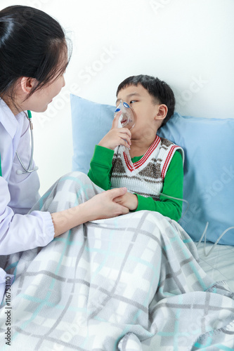 Asian boy having respiratory illness helped by health professional with inhaler.