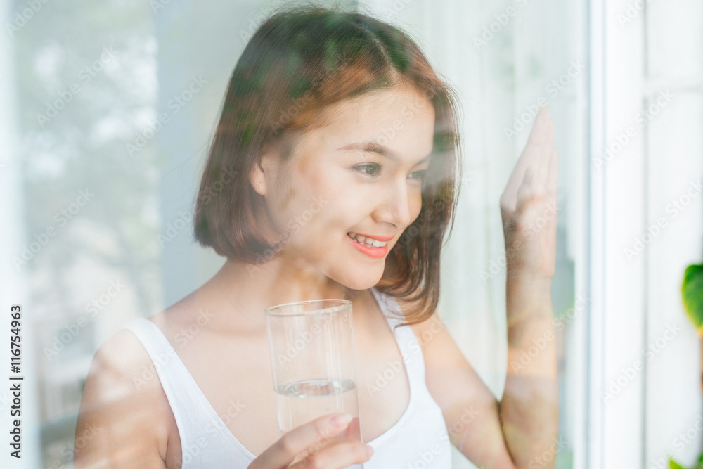 Young asian woman drinking water looking through the window Young asian woman drinking water looking through the window