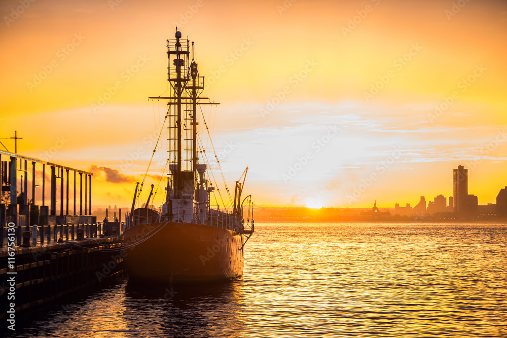 Cargo ship in the harbor at commercial port at sunset time. Sun is going down against beautiful sky at the dock with mooring vessel..