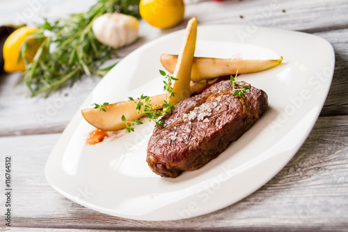 Brown meat on white plate. Salt and green herb. Ribey steak with sweet pear. Meat dish with barbecue sauce. photo