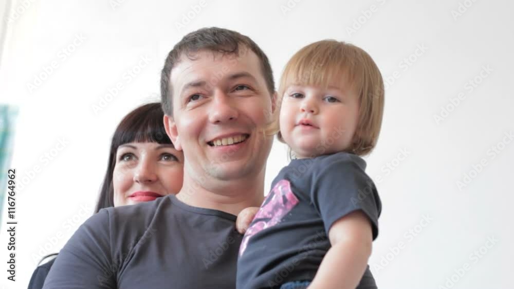 Smiling father with baby and mother behind him posing at camera