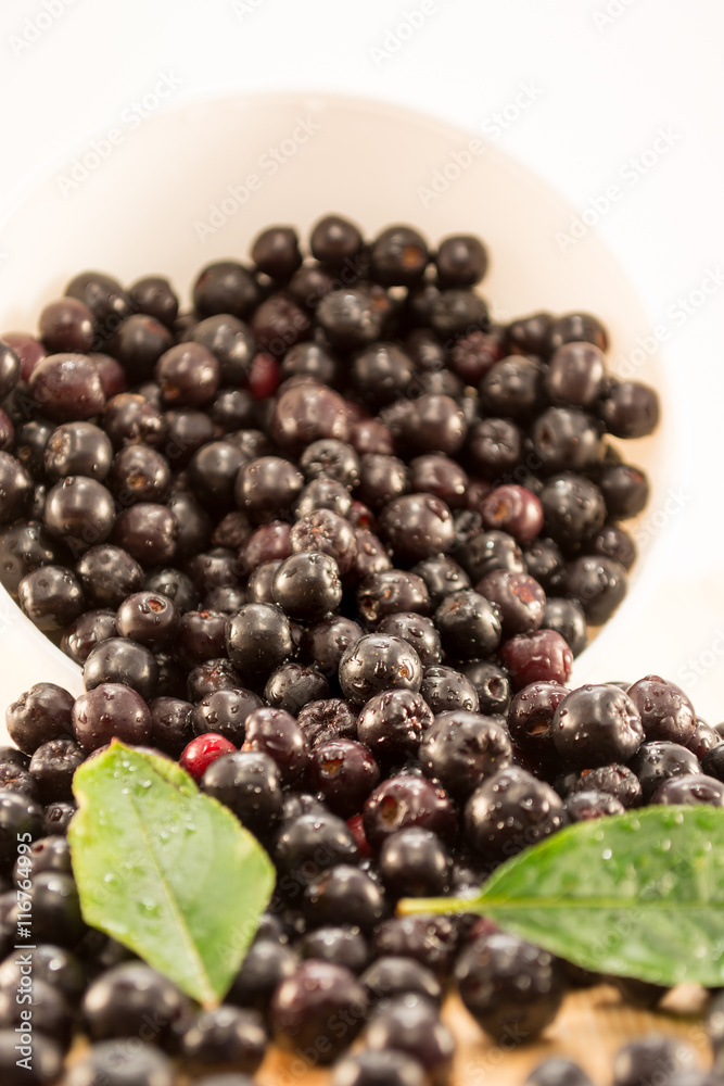 Bowl full of aronia spilled on wooden table Bowl full of aronia spilled on wooden table