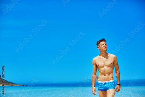 strong athletic man with bared torso standing on the beach along the sea front