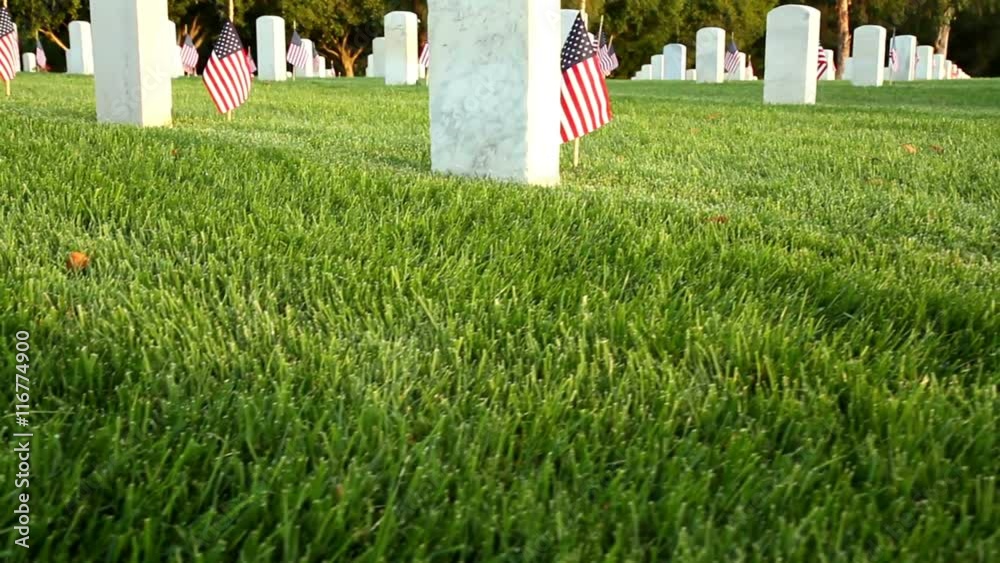 Dolly camera moves up past a marble tombstone at a US National Cemetery. Many more tombstones can be seen in the background.