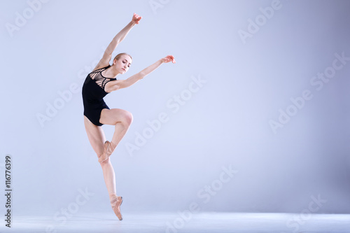 Ballet Perfection. Young and beautiful ballerina in a black dancing suit is posing in a white studio full of light.