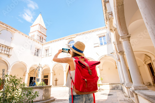 Young female traveler photographing with phone old monastery in Piran town. Traveling in Slovenia