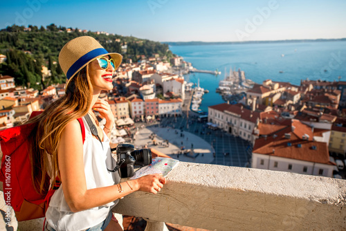 Young female traveler with red backpack and hat enjoying the view from George's tower on Piran old town. Traveling in Slovenia