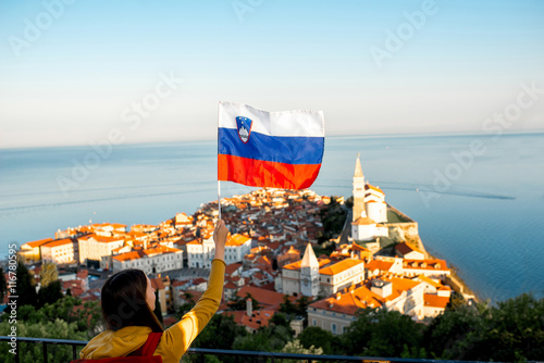 Young woman waving slovenian flag on Piran coastal town background. Promoting tourism in Slovenia photo