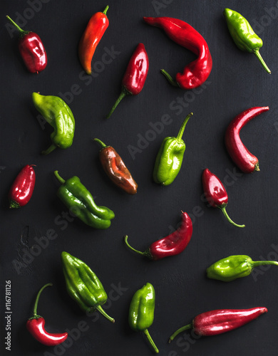 Pattern of small colorful hot chili peppers on black background, top view, vertical