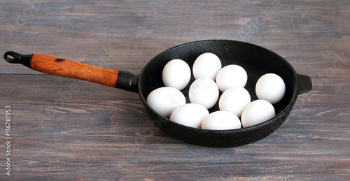 You can't make omelet without breaking eggs. Metaphor. White whole (unbroken) eggs on a cast iron pan photo
