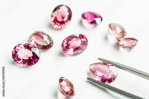 Pink Sapphire held by a pair of tweezers above some other sapphi