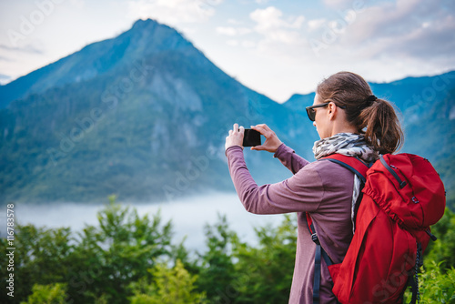 Woman hiking on the mountain and taking pictures with smart phon
