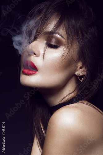 Beautiful sexy brunette girl with bright makeup  red lips  smoke from mouth. beauty face.
