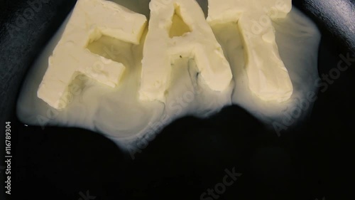Butter in shape of the word fat melting on hot pan - Close up top view.