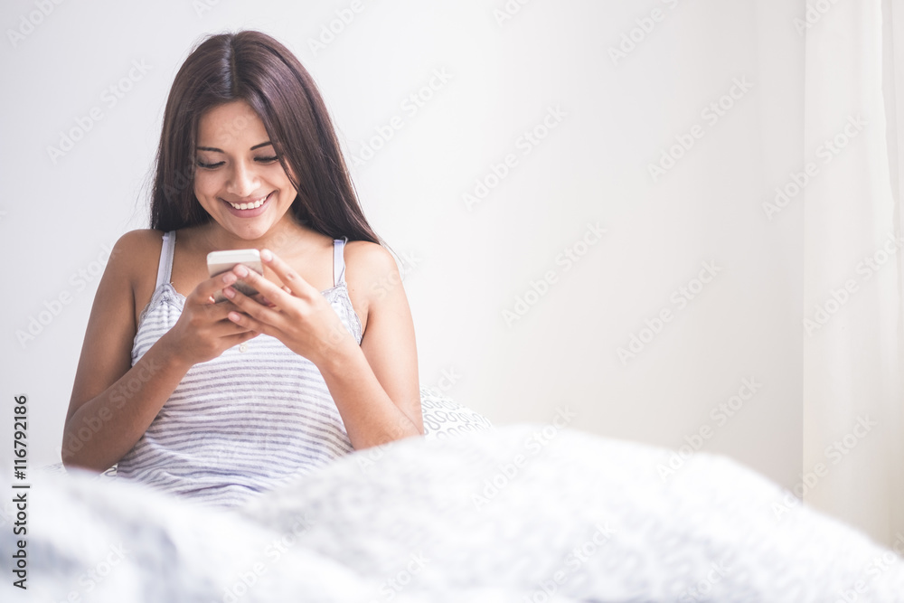 Teenage girl waking up, reading message on smartphone Teenage girl waking up, reading message on smartphone