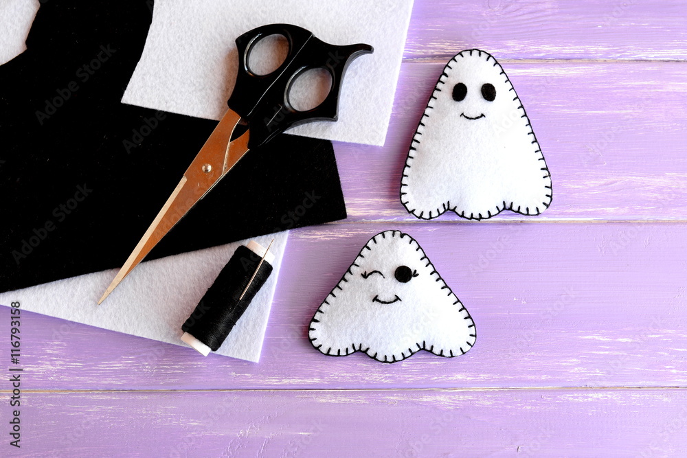 Two small white ghosts crafts, felt sheets, scissors, thread, needle on  lilac wooden background. Hand Halloween decor idea for kids. Halloween  sewing craft Photos