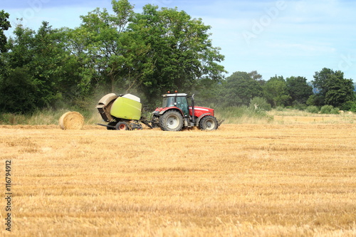 Red tractor in corn field bailing hay