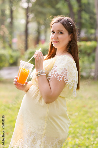 the beautiful young pregnant woman with juice in park in summer day