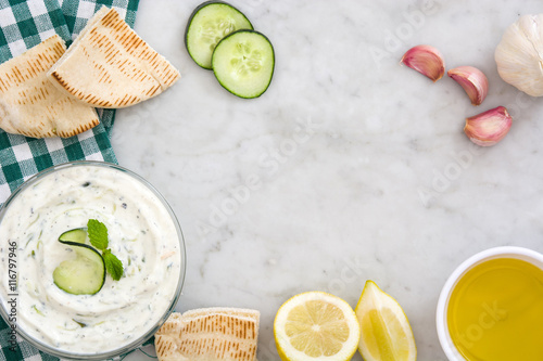 Tzatziki in bowl and ingredients on white marble 