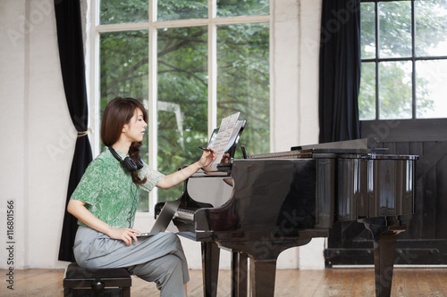Young woman sitting at a grand piano in a rehearsal studio, annotating sheet music.