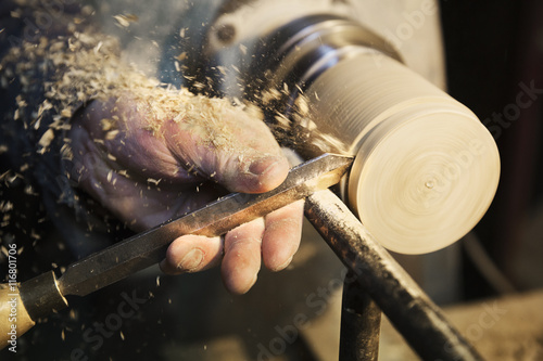 Man standing at a woodworking machine in a carpentry workshop, turning a piece of wood.