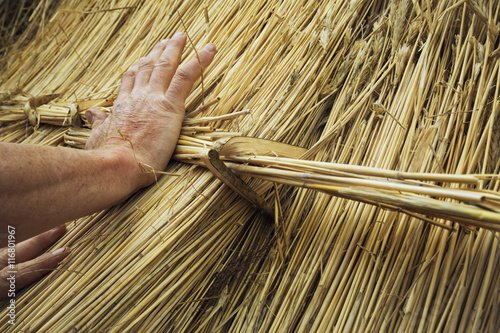 Close up of a man thatching a roof, fastening a bundle of straw with a hazel wood peg. photo