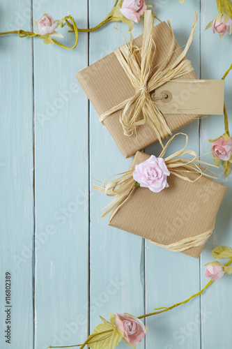 Presents wrapped in brown paper with pink roses on a rustic blue wooden background forming a page border