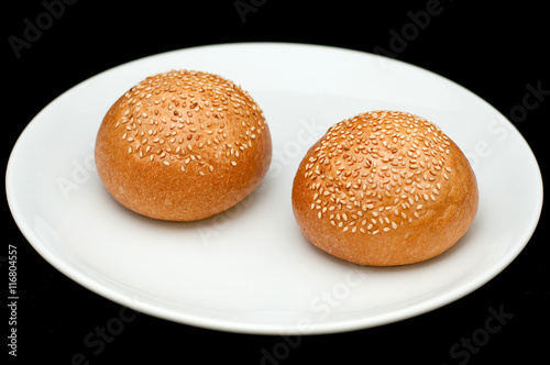 Two sandwich buns with sesame on white plate