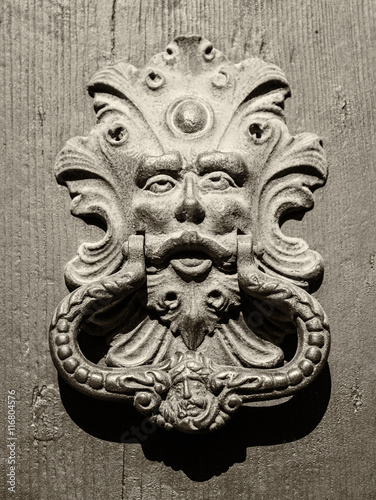 Antique door knocker of an old door in Italy.